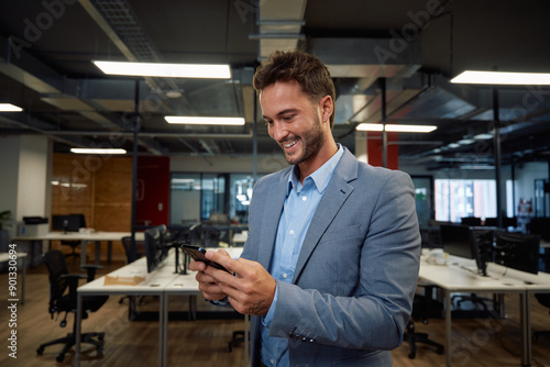 Happy young caucasian man in businesswear using mobile phone in office