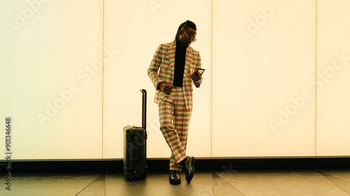 Businessman using smart phone standing by luggage near illuminated wall