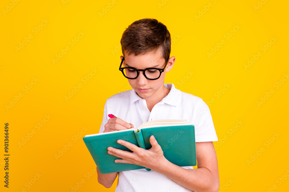 Photo of good mood school boy wear white t-shirt writing copybook emtpy space isolated yellow color background Photo of good mood school boy wear white t-shirt writing copybook emtpy space isolated yellow color background