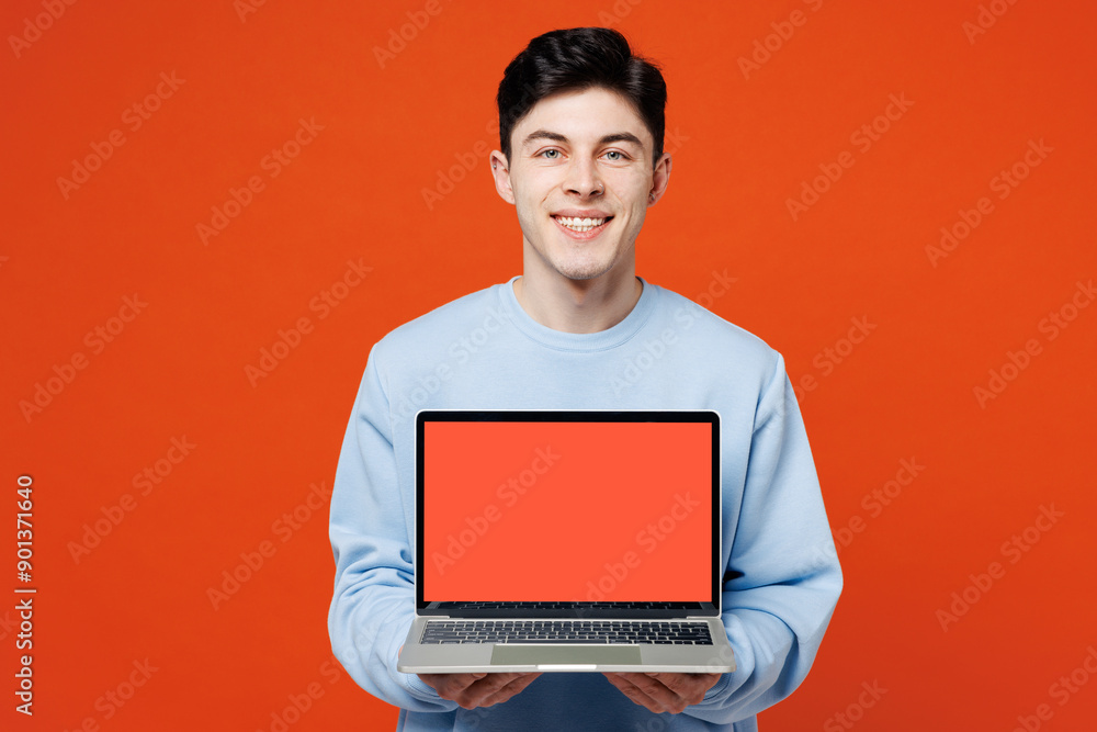Young IT man wears blue sweatshirt casual clothes hold use work on laptop pc computer with blank screen workspace area isolated on plain red orange color background studio portrait. Lifestyle concept. Young IT man wears blue sweatshirt casual clothes hold use work on laptop pc computer with blank screen workspace area isolated on plain red orange color background studio portrait. Lifestyle concept.