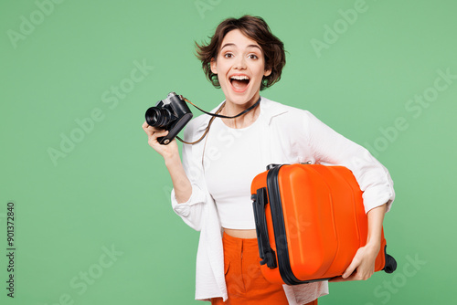 Fotografie Traveler surprised shocked woman wear casual clothes hold suitcase bag photo camera isolated on plain green background