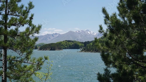 Tranquil Mountain lake at spring trees moving from wind slow motion Snow covered mountains Background sunny day photo