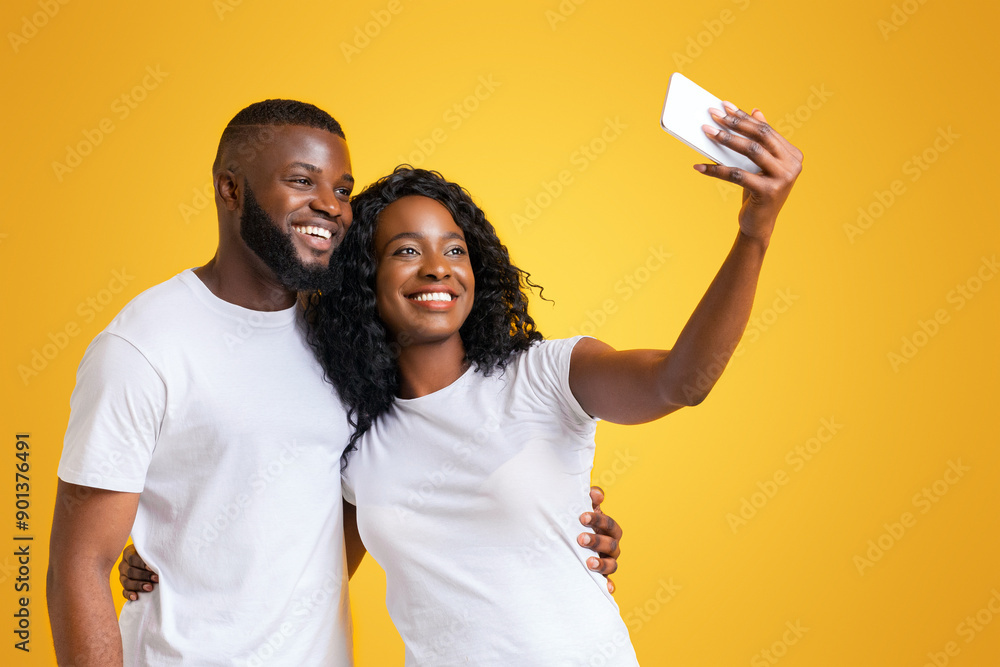 A couple smiles for a selfie, the woman holding a phone up to take the picture. A couple smiles for a selfie, the woman holding a phone up to take the picture.