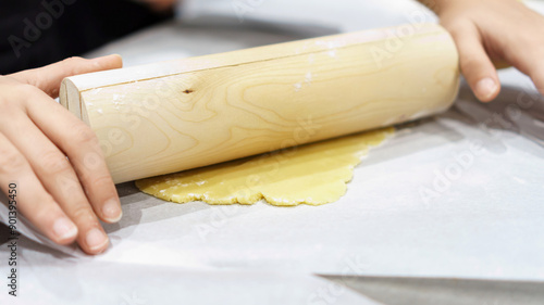 Teenage hands deftly rolling out dough with a wooden rolling pin, capturing the artisanal steps involved in crafting homemade baked goods. photo