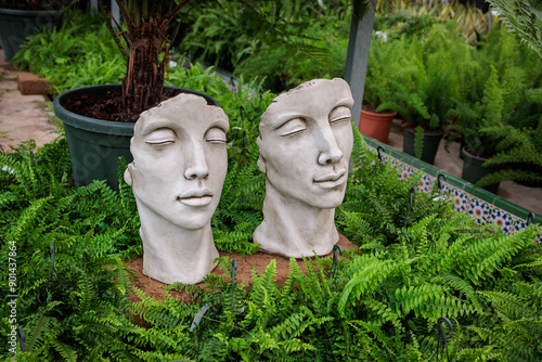 Fotografía Two stone busts resting on ferns in garden center