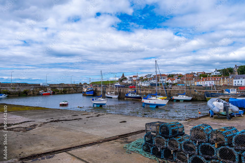 St Monans Harbour on the east coast of Scotland on the Fyfe coast  looking over lobster pots to the boats and the sea defences with the ancient church of the same name in the far distance.