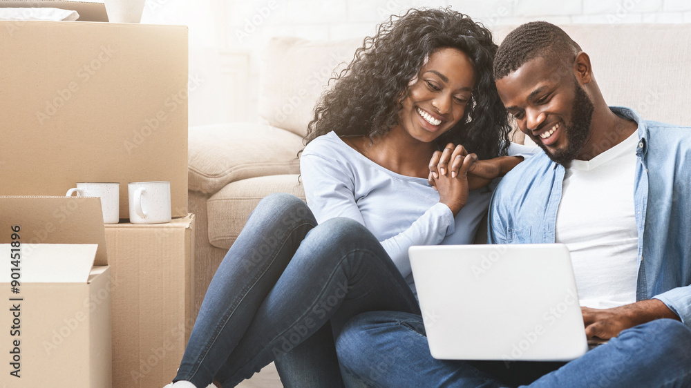Smiling african couple sitting on floor at new apartment, choosing new furniture online, using laptop, copy space Smiling african couple sitting on floor at new apartment, choosing new furniture online, using laptop, copy space