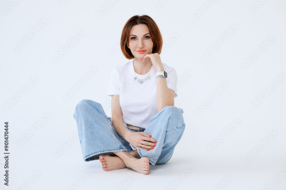 Attractive middle-aged woman in jeans and barefoot on a white background. Portrait of a woman in casual clothes. Attractive middle-aged woman in jeans and barefoot on a white background. Portrait of a woman in casual clothes.