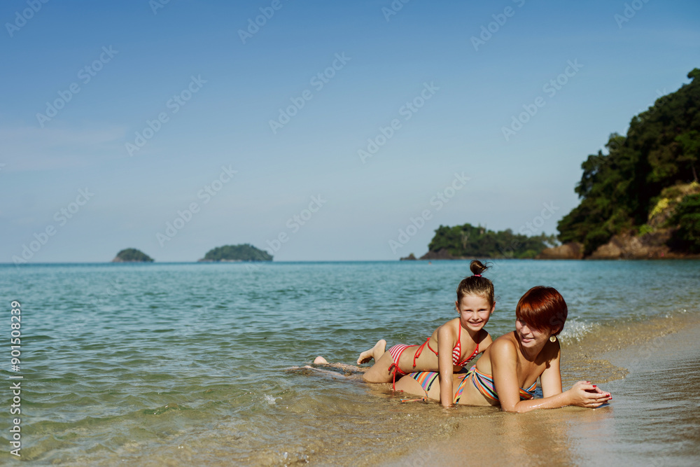 Mom and daughter are lying on the shore on the beach in the water. They're laughing. Rest, vacation, happiness Mom and daughter are lying on the shore on the beach in the water. They're laughing. Rest, vacation, happiness