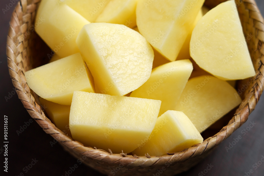 Raw potatoes, freshly cut into wedges, are arranged in a wicker basket on brown board Raw potatoes, freshly cut into wedges, are arranged in a wicker basket on brown board