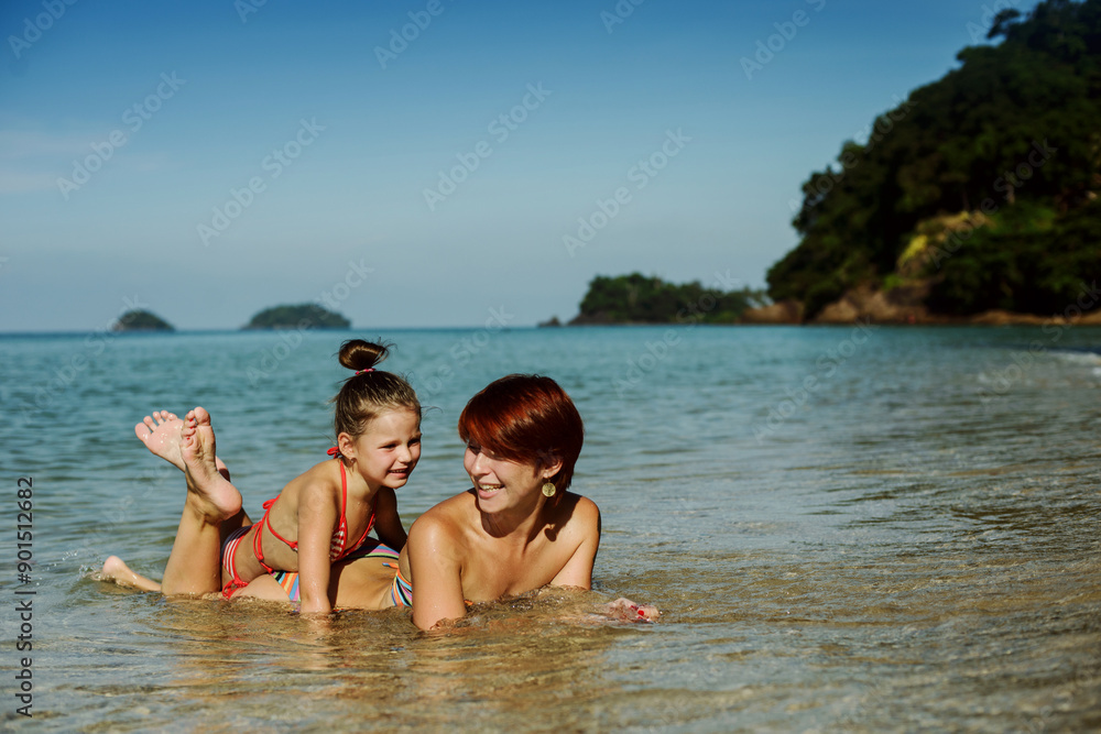 Mom and daughter are lying on the shore on the beach in the water. They're laughing. Rest, vacation, happiness Mom and daughter are lying on the shore on the beach in the water. They're laughing. Rest, vacation, happiness