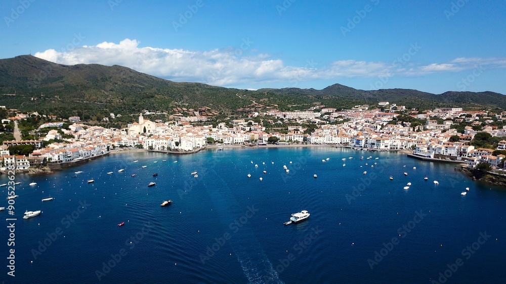 Naklejka premium aerial view over the Badia de Cadaqués, to the old white houses of Cadaqués, Port Alguer and the turquoise water of the Mediterranean Sea, mountains of the Pyrenees behind, Girona, Catalonia, Spain