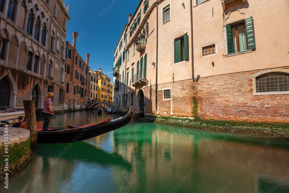 Venice, Italy - June 05, 2024: A gondolier is waiting for tourists on the bridge over the canal. Popular tourist attractions in Venice. Long exposure shot. Venice, Italy - June 05, 2024: A gondolier is waiting for tourists on the bridge over the canal. Popular tourist attractions in Venice. Long exposure shot.