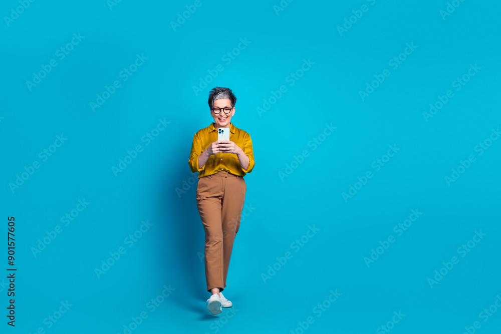Full length photo of adorable good mood lady dressed shirt eyewear typing modern gadget empty space isolated blue color background Full length photo of adorable good mood lady dressed shirt eyewear typing modern gadget empty space isolated blue color background