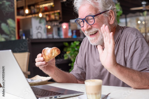 фотографія Elderly man in video call while enjoying breakfast with coffee and pastry at a cafe