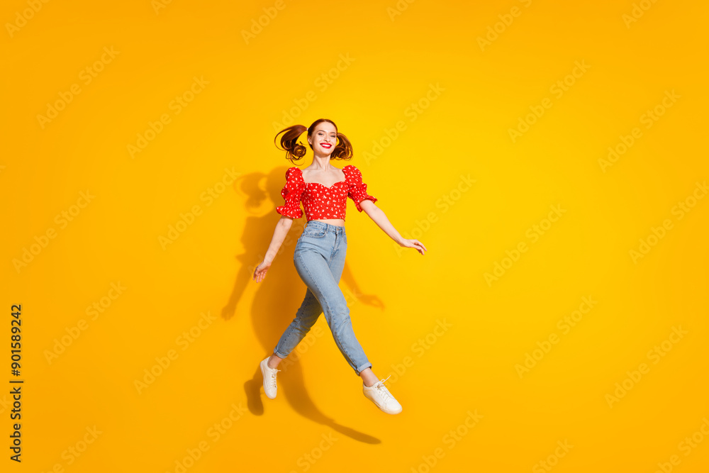 Photo portrait of young red hair funky positive girl wearing blouse and jeans running jumping carefree isolated on yellow color background Photo portrait of young red hair funky positive girl wearing blouse and jeans running jumping carefree isolated on yellow color background