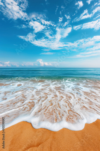 Vibrant ocean waves gently rolling onto a golden sandy beach under a bright blue sky with scattered clouds, capturing the essence of a perfect beach day.