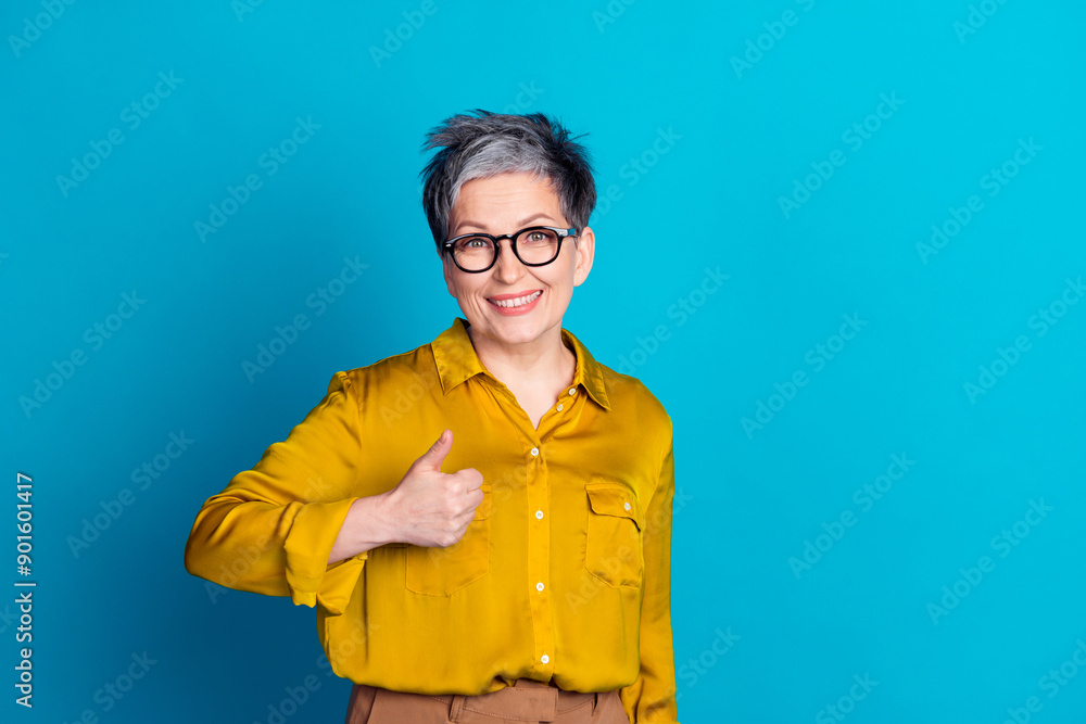 Photo of charming positive woman wear blouse eyeglasses showing thumb up empty space isolated blue color background Photo of charming positive woman wear blouse eyeglasses showing thumb up empty space isolated blue color background