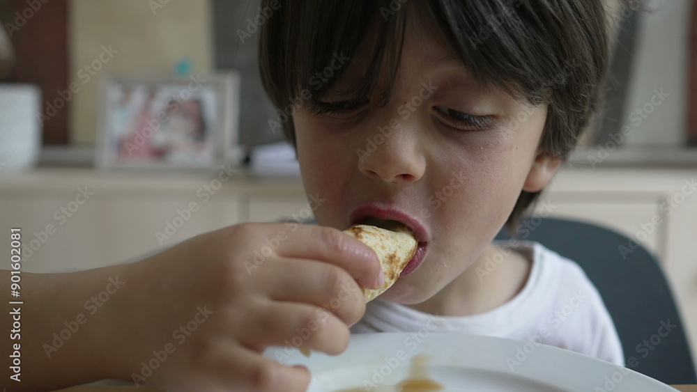 Young boy enjoys a tasty pancake, focusing on the flavor with a serious expression, highlighting a precious and candid dining moment at home Young boy enjoys a tasty pancake, focusing on the flavor with a serious expression, highlighting a precious and candid dining moment at home