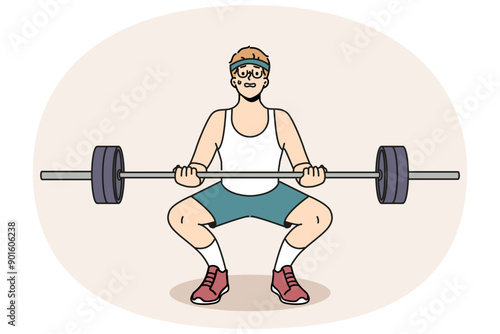 Man with barbell goes in for sports in gym, wanting to have beautiful figure and healthy body. Guy novice bodybuilder squats with barbell in hands and needs help of fitness trainer.