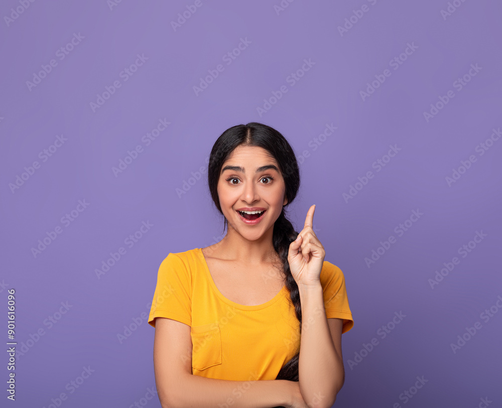 Inspiration, Creativity, Solution, Eureka concept. Portrait of excited young indian woman in yellow t-shirt raising finger up and smiling, having wow creative idea, purple studio background, copyspace