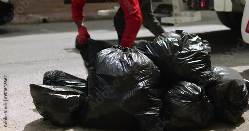 Black man throws trash packs into garbage truck on city street closeup. Yard keeper throws sacks with rubbish into lorry trailer. Waste collecting