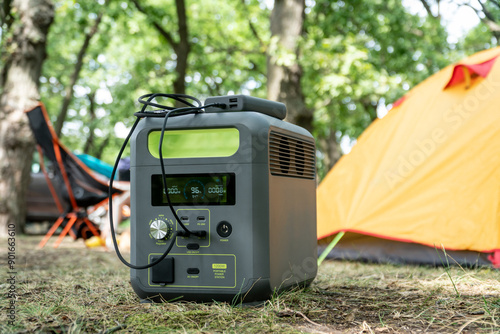 Portable power station with lithium ferrophosphate battery  charging electronic  devices used at a wild camp site,  in front  of yellow tent photo