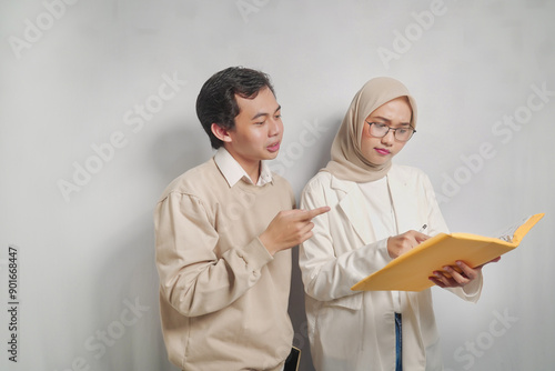 A young man points to a document while a woman in a headscarf reads it.