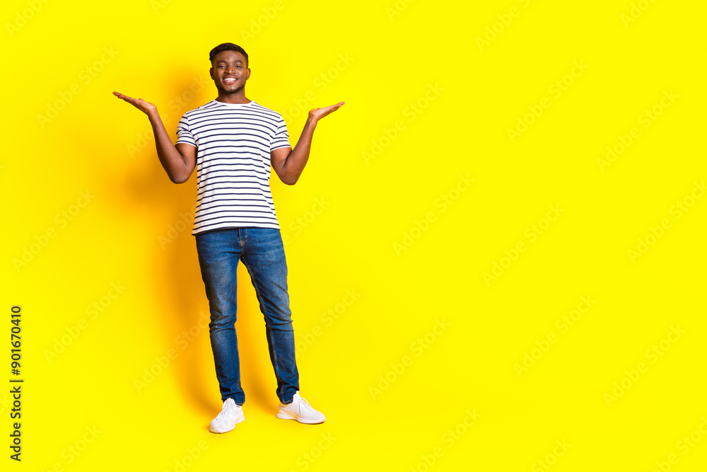 Full size photo of nice young man hold empty space vs wear t-shirt isolated on bright yellow color background Full size photo of nice young man hold empty space vs wear t-shirt isolated on bright yellow color background