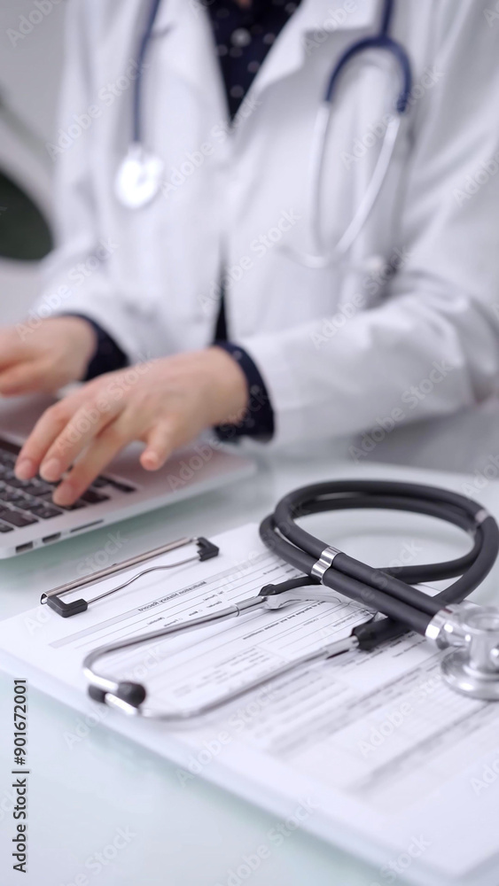 Stethoscope is lying on the glass table while doctor woman is working with laptop computer on the background, close-up. Medicine and pharmacy concept