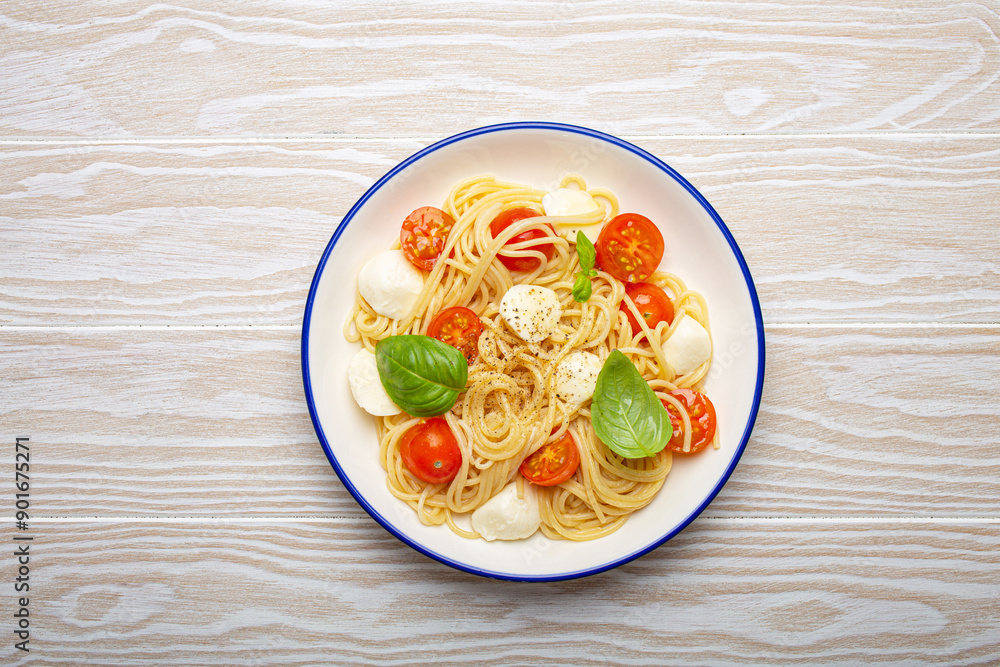 Delicious spaghetti with tomatoes and mozzarella cheese served on white wooden table with cutlery aside, top view Delicious spaghetti with tomatoes and mozzarella cheese served on white wooden table with cutlery aside, top view