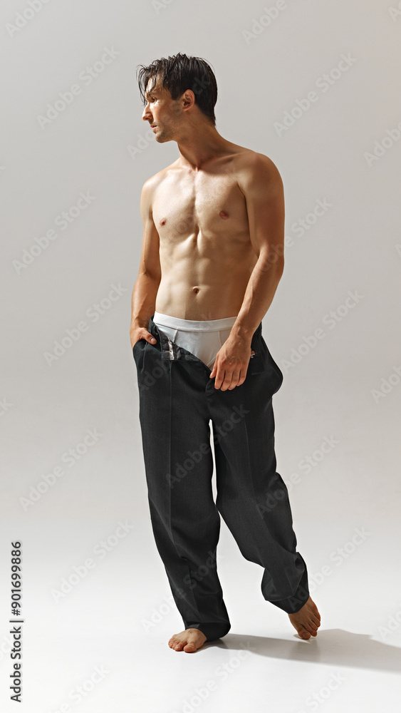 Full-length portrait of handsome young man with muscular relief, athletic body, posing shirtless in black pants isolated on light studio background. Concept of male beauty, body and health care. sport Full-length portrait of handsome young man with muscular relief, athletic body, posing shirtless in black pants isolated on light studio background. Concept of male beauty, body and health care. sport