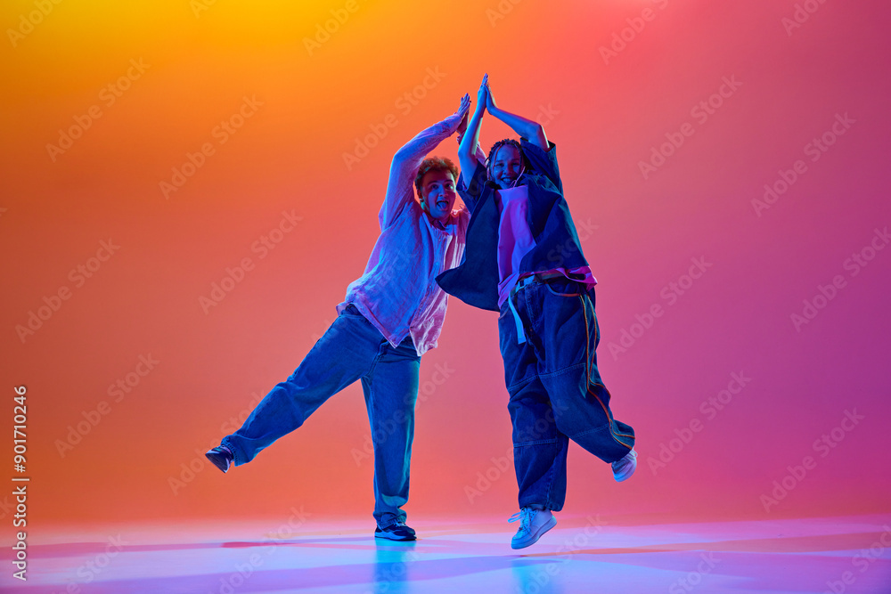 Young people, man and woman, dancers performing modern dance styles, dancing hip-hop against gradient studio background in neon light. Concept of contemporary dance, hobby, youth Young people, man and woman, dancers performing modern dance styles, dancing hip-hop against gradient studio background in neon light. Concept of contemporary dance, hobby, youth