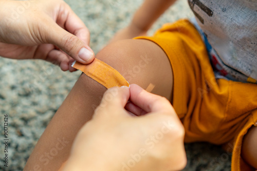 A mother is applying a band-aid to a scrape on her child's leg, who fell while playing in the park, first aid concept