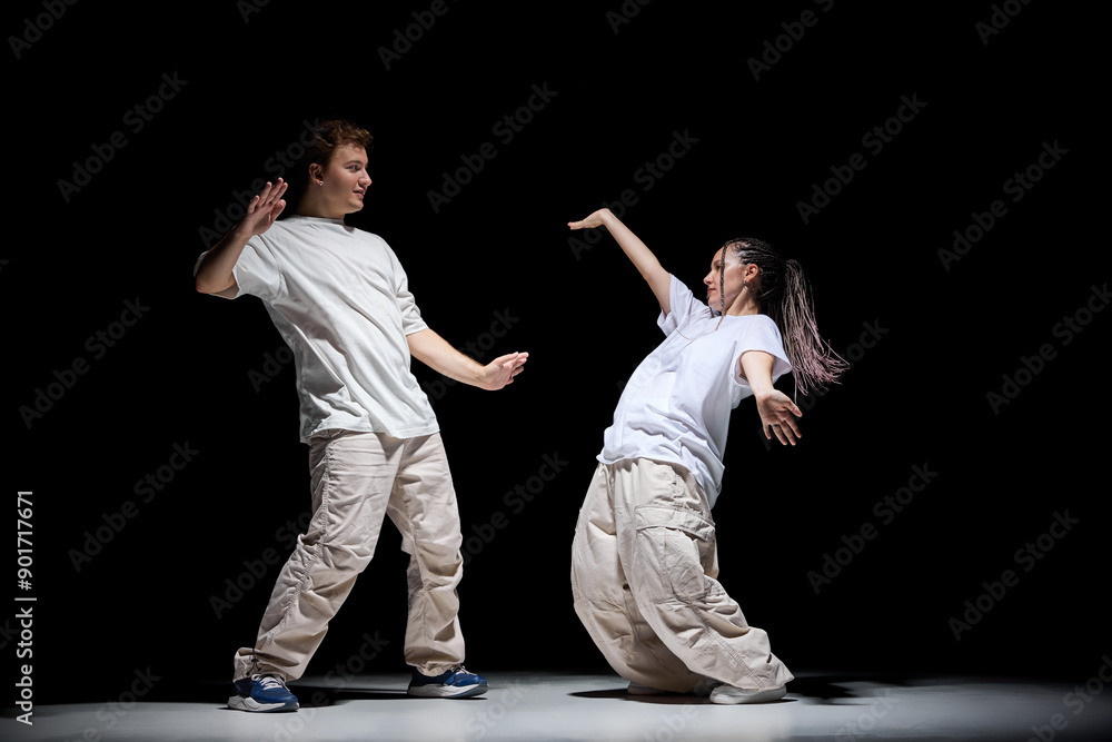 Freestyle. Imagination. Young talented man and woman in light clothes dancing hip-hop against black studio background. Concept of contemporary dance, hobby, youth, entertainment Freestyle. Imagination. Young talented man and woman in light clothes dancing hip-hop against black studio background. Concept of contemporary dance, hobby, youth, entertainment