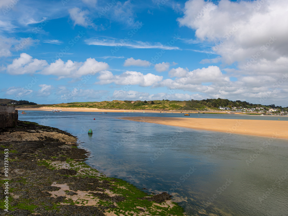 River Camel estuary between Padstow and Rock in Cornwall, England. Seaweed covers foreground shore. Shows sandbank and grassy hills in background. Cloudy blue sky. River Camel estuary between Padstow and Rock in Cornwall, England. Seaweed covers foreground shore. Shows sandbank and grassy hills in background. Cloudy blue sky.