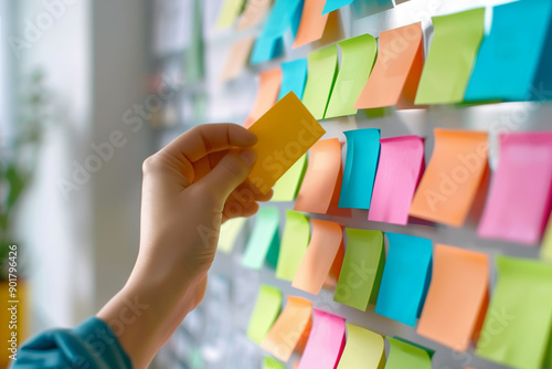 Clean photo of a person arranging colorful sticky notes on a wall, symbolizing brainstorming