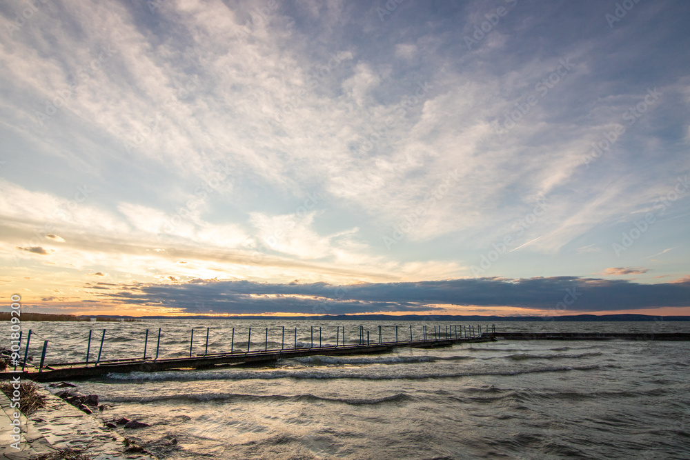 Water landscape taken from the shore of a calm lake. View over the reflecting water to the horizon in the sunset. a jetty or pier at Siofok harbor, Balaton, Hungary Water landscape taken from the shore of a calm lake. View over the reflecting water to the horizon in the sunset. a jetty or pier at Siofok harbor, Balaton, Hungary