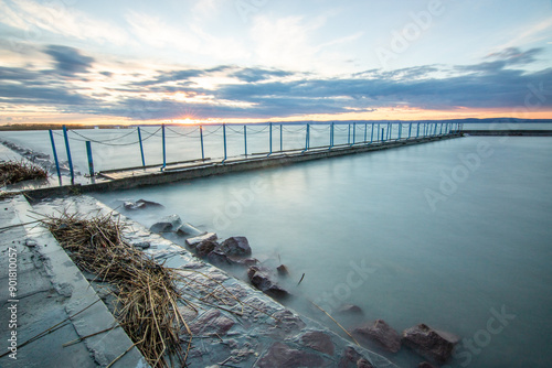 Water landscape taken from the shore of a calm lake. View over the reflecting water to the horizon in the sunset. a jetty or pier at Siofok harbor, Balaton, Hungary photo