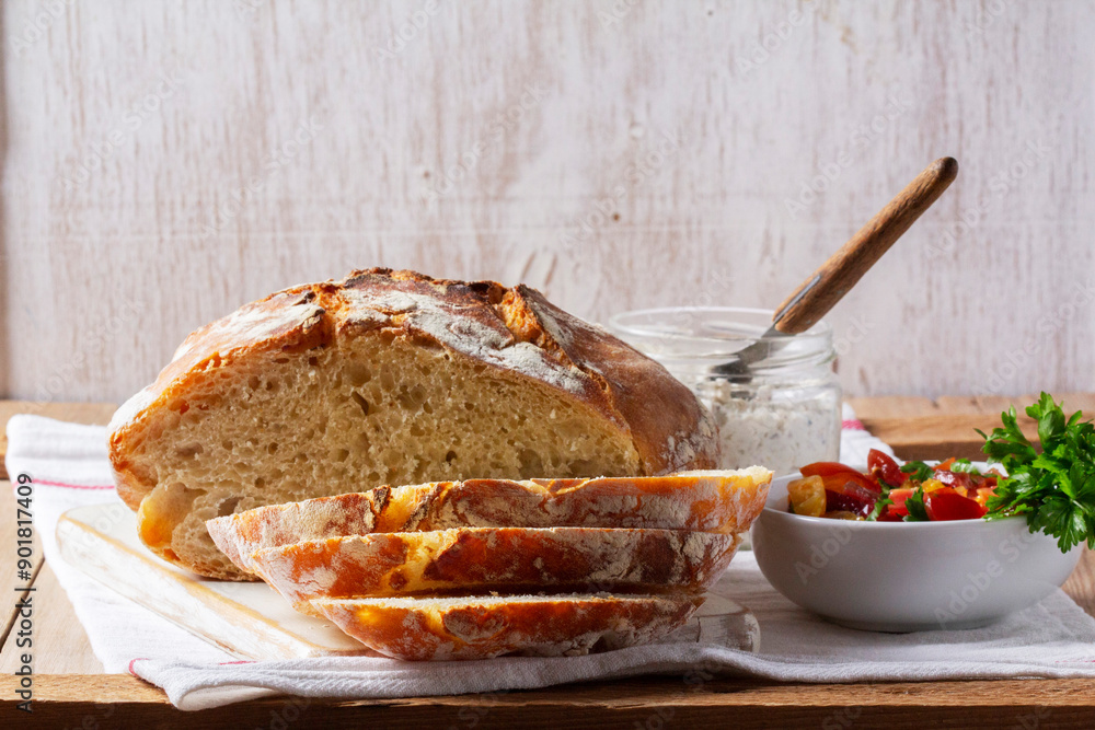 Round yeast bread made from white and whole grain flour, tomato salad and pate on a wooden background. Rustic style.