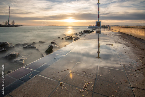 a small marina on a lake. Breakwater and pillar with golden figure in the dreamy sunset. Landscape shot in Siófok, Balaton, Hungary photo