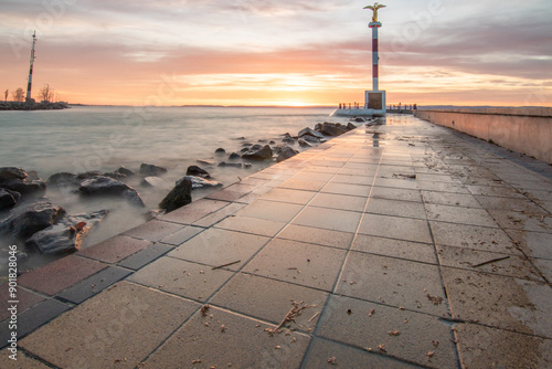 a small marina on a lake. Breakwater and pillar with golden figure in the dreamy sunset. Landscape shot in Siófok, Balaton, Hungary photo