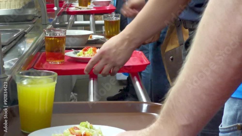 Cafeteria customers choose food and move trays with plates towards the cash register. Fast food concept in a restaurant or cafeteria.
