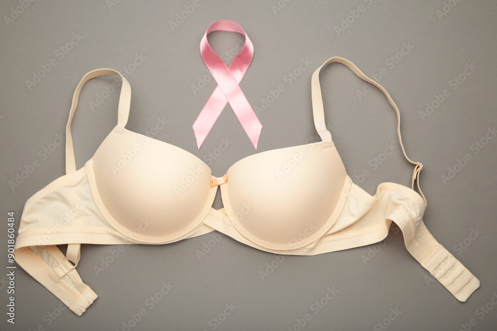 Breast Cancer Awareness Ribbon. Beige bra and pink ribbon tape lying on female bra on grey backgrounds. Breast cancer awareness and October Pink day, world cancer day. Breast Cancer Awareness Ribbon. Beige bra and pink ribbon tape lying on female bra on grey backgrounds. Breast cancer awareness and October Pink day, world cancer day.