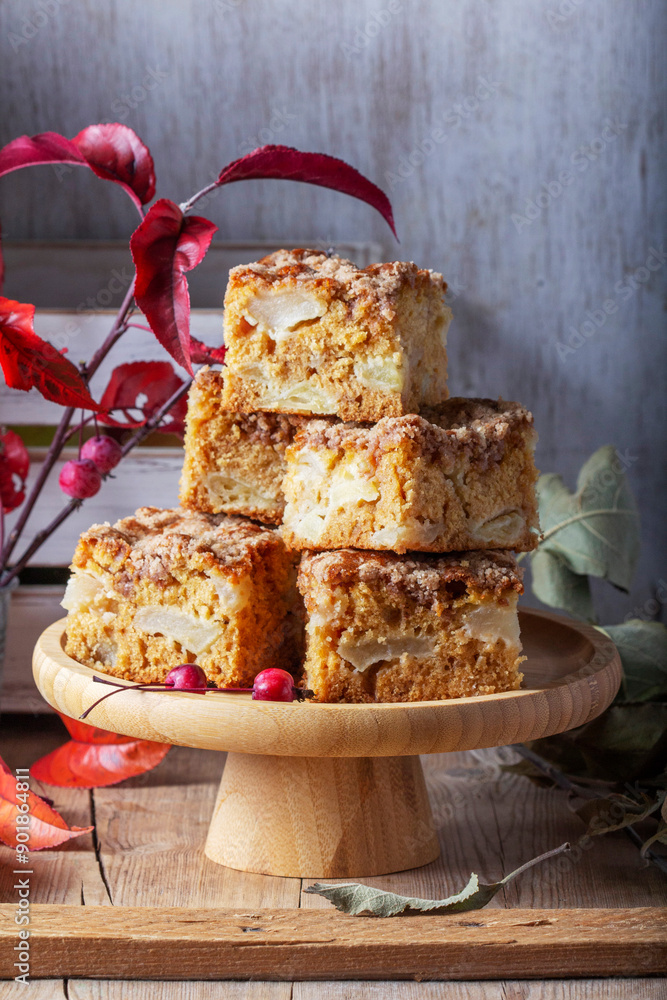 Slices of Dutch apple cake with streusel on a wooden tray, apples and apple branches on a wooden background.