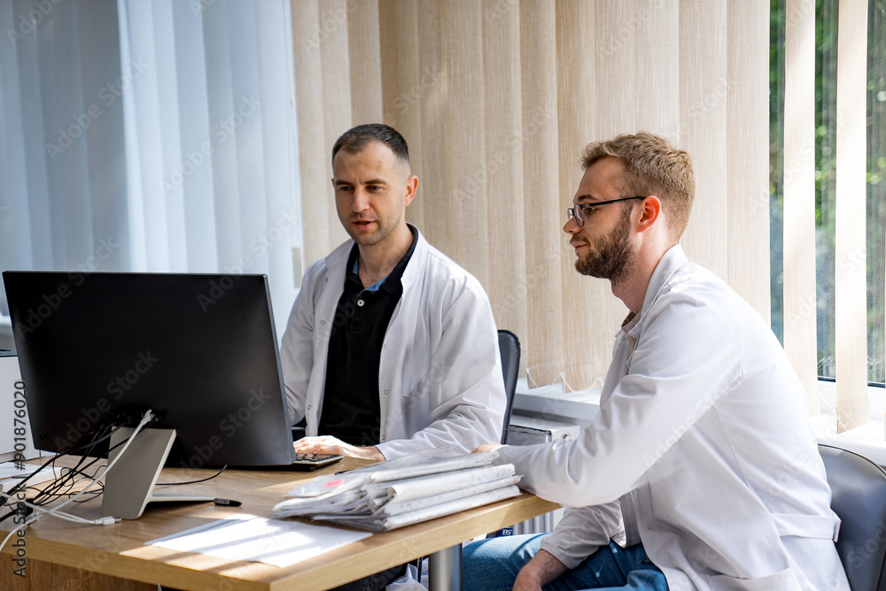 Two Doctors Working on Computer in Office. Two doctors are working at a desk in an office, looking at a computer screen. Two Doctors Working on Computer in Office. Two doctors are working at a desk in an office, looking at a computer screen.