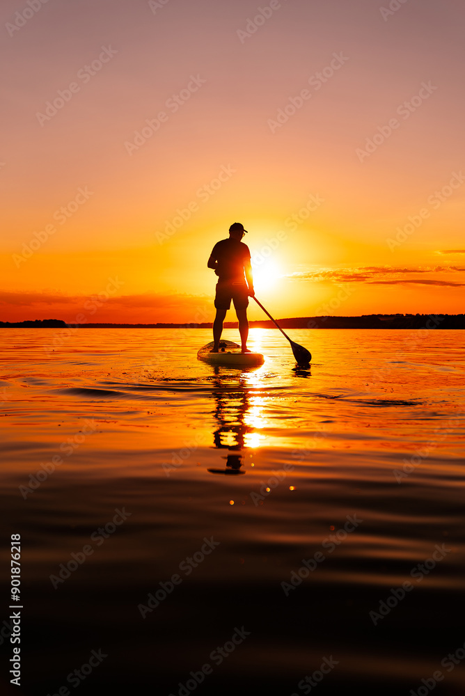 Paddleboarding at Sunset. A single person paddleboards on a still lake as the sun sets behind them, creating a beautiful orange glow across the water.