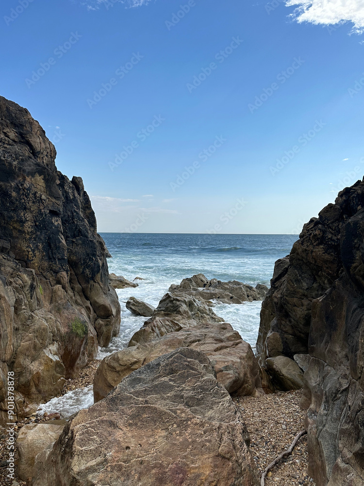 Rugged coastal rocks frame the view of a tranquil ocean under a bright blue sky, the waves gently crashing against the shore, embodying the raw, untamed beauty of Portugal's coastline. Rugged coastal rocks frame the view of a tranquil ocean under a bright blue sky, the waves gently crashing against the shore, embodying the raw, untamed beauty of Portugal's coastline.