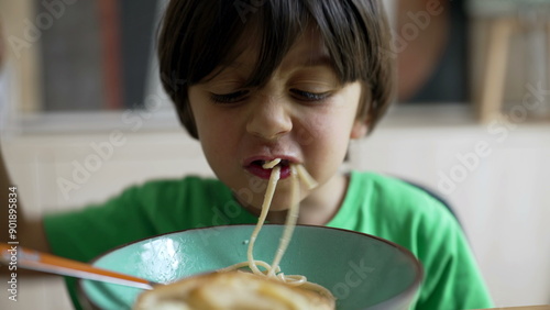 Young boy playfully eating a bowl of pasta, making funny faces and acting goofy, capturing the joy and silliness of childhood during mealtime
