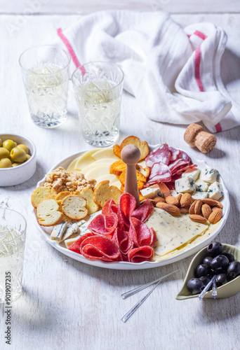 Aperitif, champagne and snack of sausage, cheese, nuts, olives and crackers on a light background.